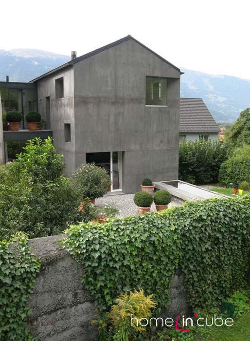Viditelný jasný kontrast šedivého betonového fasádního systému a syté zeleně.