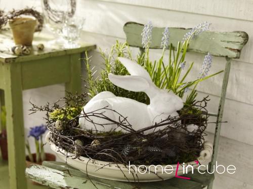 Soška zajíčka osazena do hnízda z proutí, ozdobeného jarními květy a kraslicemi jsou symbolem jarních svátků Velikonoc.